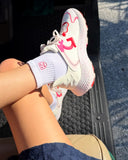 Person wearing white sneakers with pink accents and a pink logo sock, sitting on a car seat.